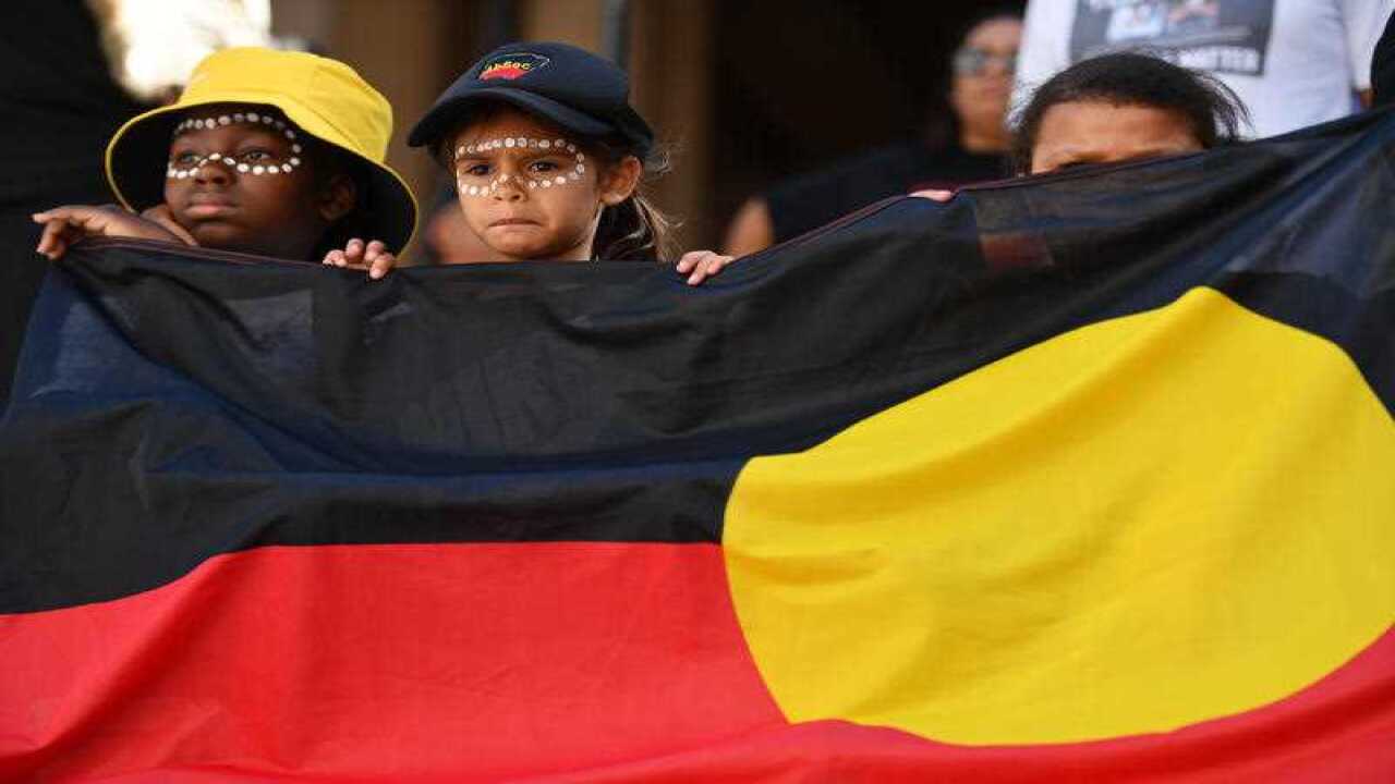 Young protestors hold an Aboriginal flag.