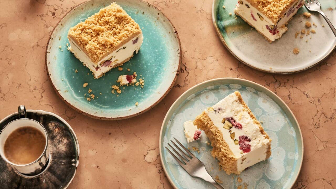 Serves of a layered ice-cream dessert sit on three different beautiful plates in tones of cream, grey and teal. A cup of tea sits nearby.