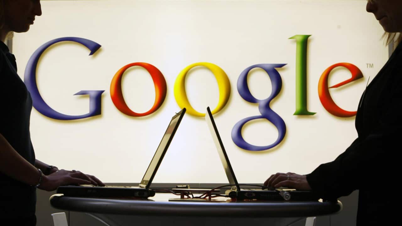 People working on laptops in front of the Google logo