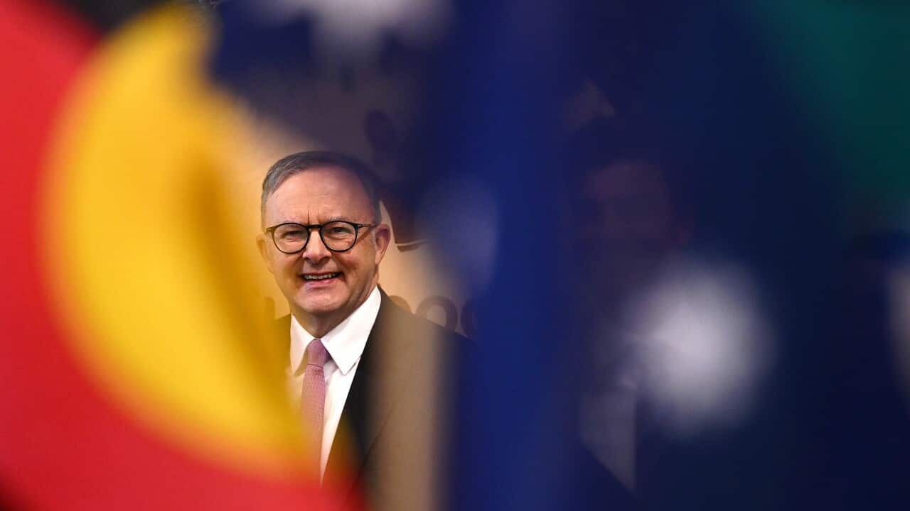 Anthony Albanese smiles, with Aboriginal and Torres Strait Islander flags in the foreground.