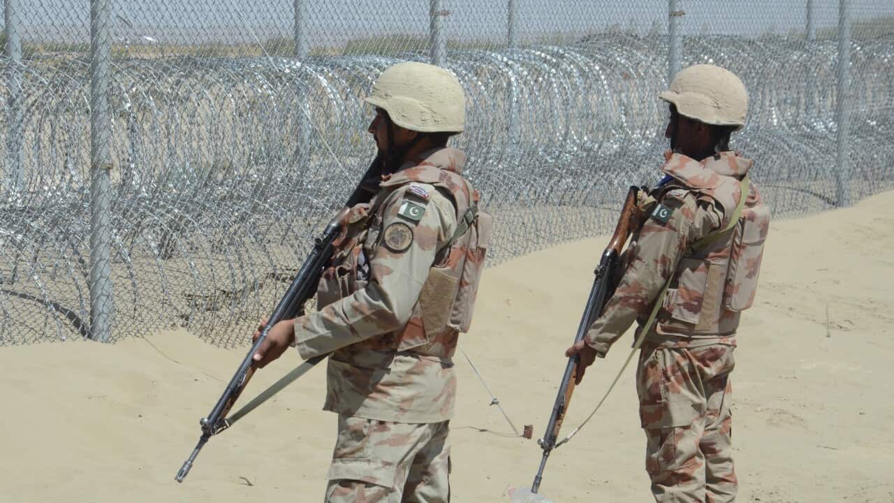 Two soldiers stand guard near a border fencing