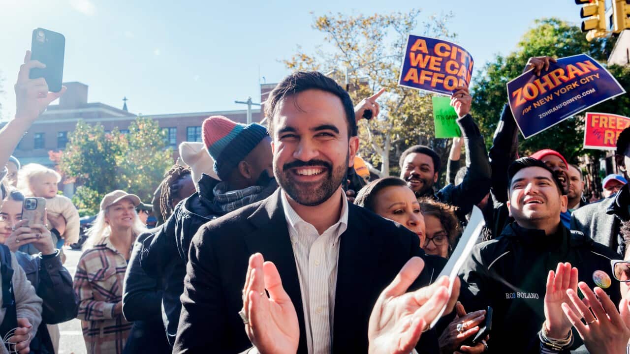 A young man wearing a dark suit and white shirt claps and smiles among a crowd of supporters.