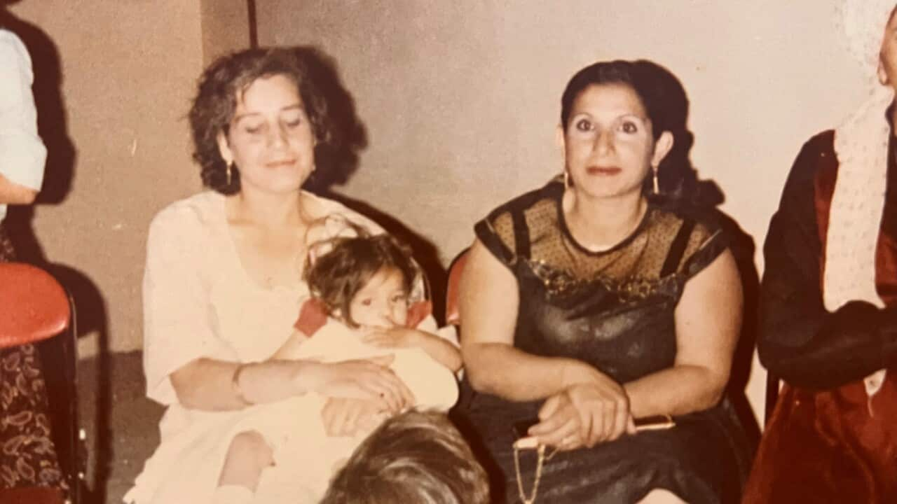 Two women sit on chairs. One is holding a young child in her arms. 