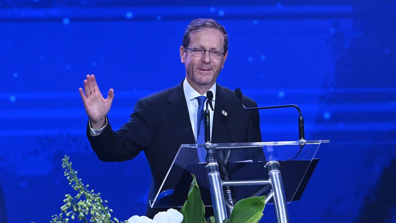 Isaac Herzog waves while speaking at a lectern against a blue background.