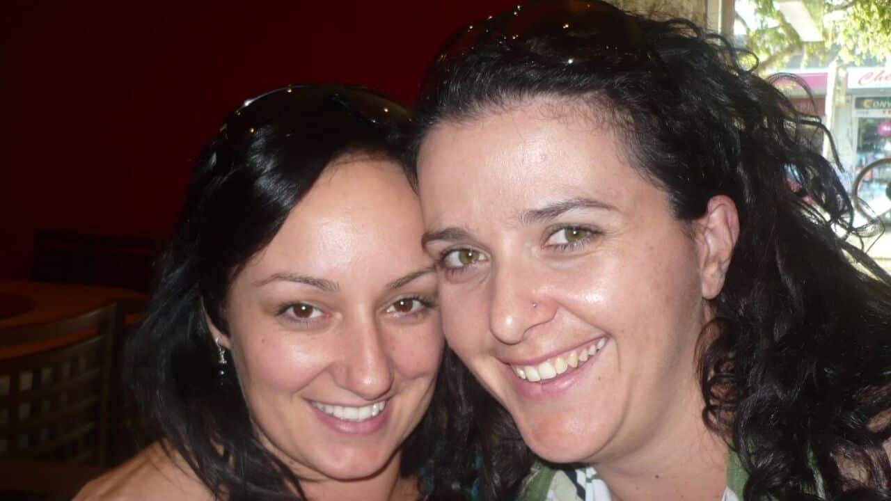 two women with dark hair and sunglasses on their heads taking a selfie and smiling into the camera in a bar