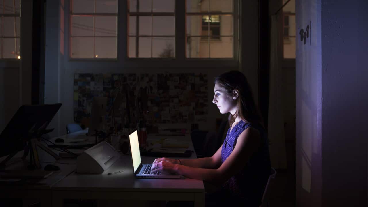 Young employee working late on computer in dark.