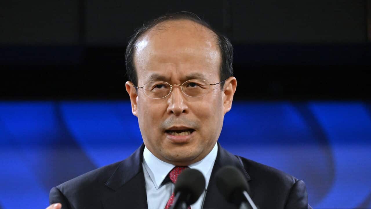 A Chinese man wearing glasses stands at a lecturn