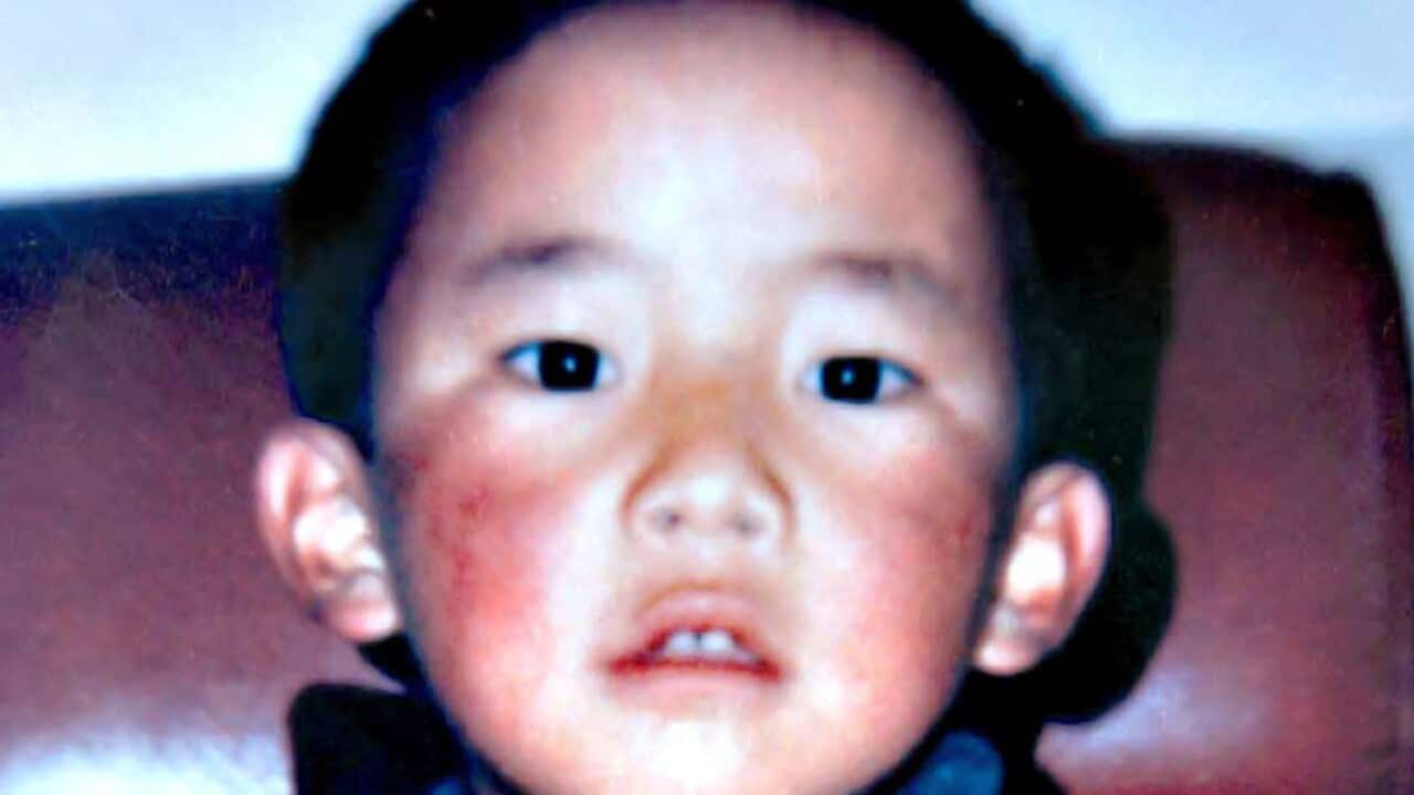 A young boy wearing an orange top looks forward