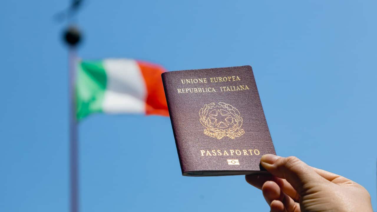 Hand holding Italian passport with Italian flag in the background
