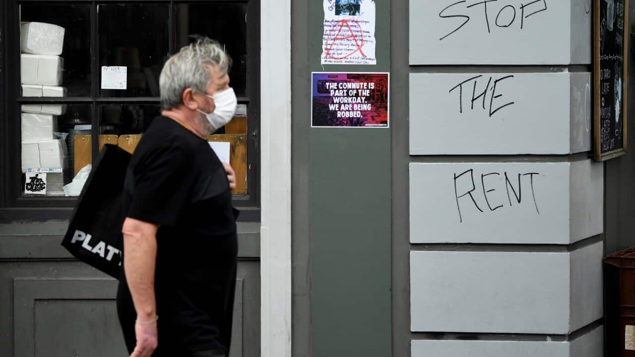 Man walks past a shop with 'Stop the Rent' sign.