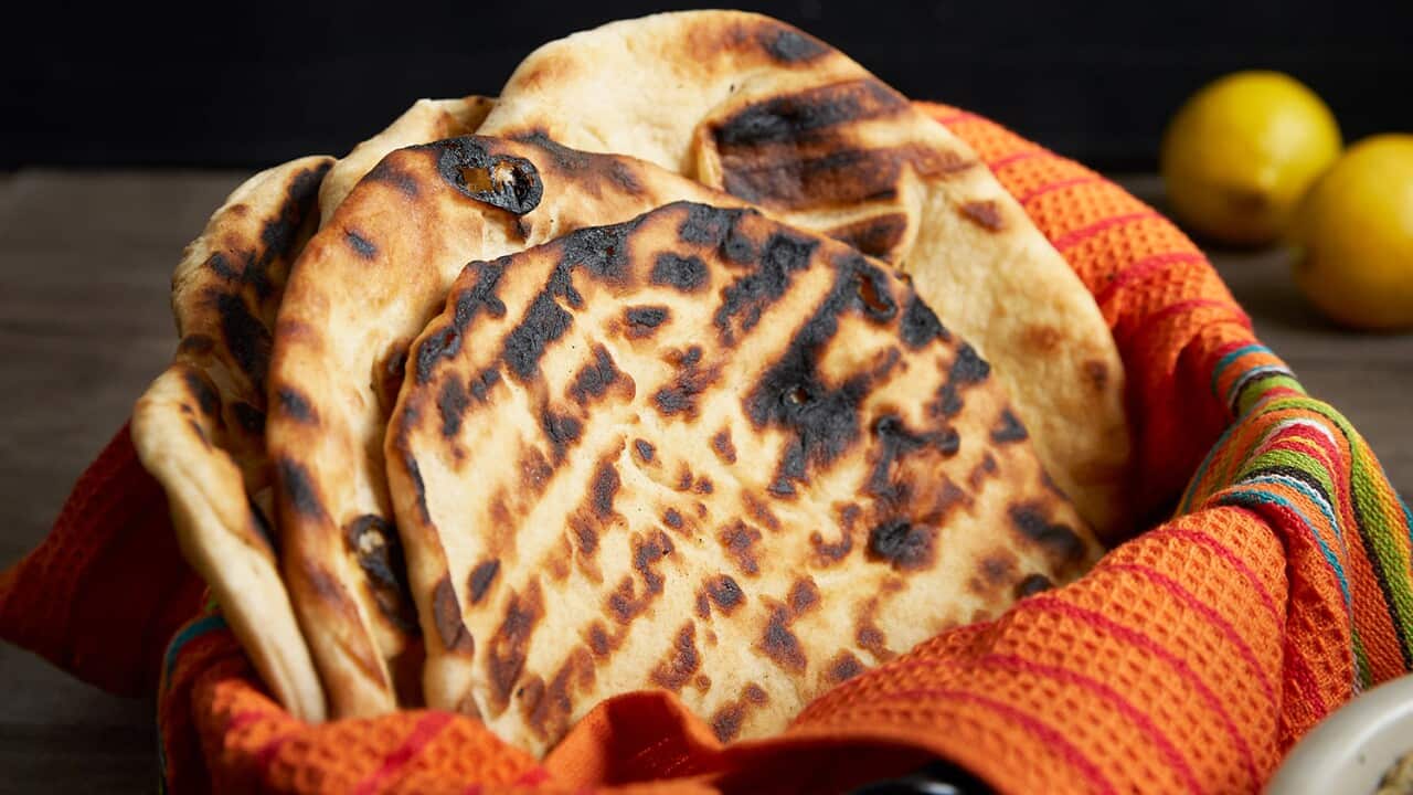 Six round flatbreads with charry grill marks sit in a container that's lined with a bright red-orange cloth.