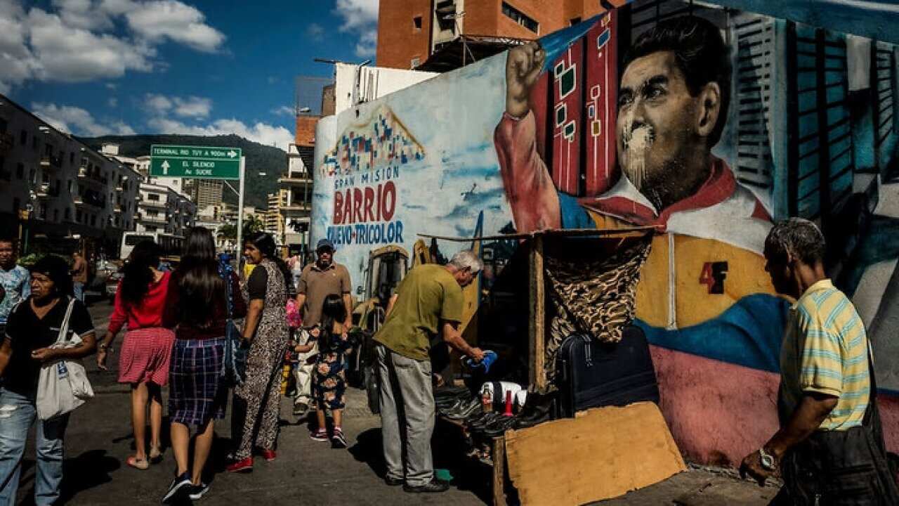 People pass a defaced mural of Venezuelan President Nicolas Maduro in the center of Caracas, Venezuela.