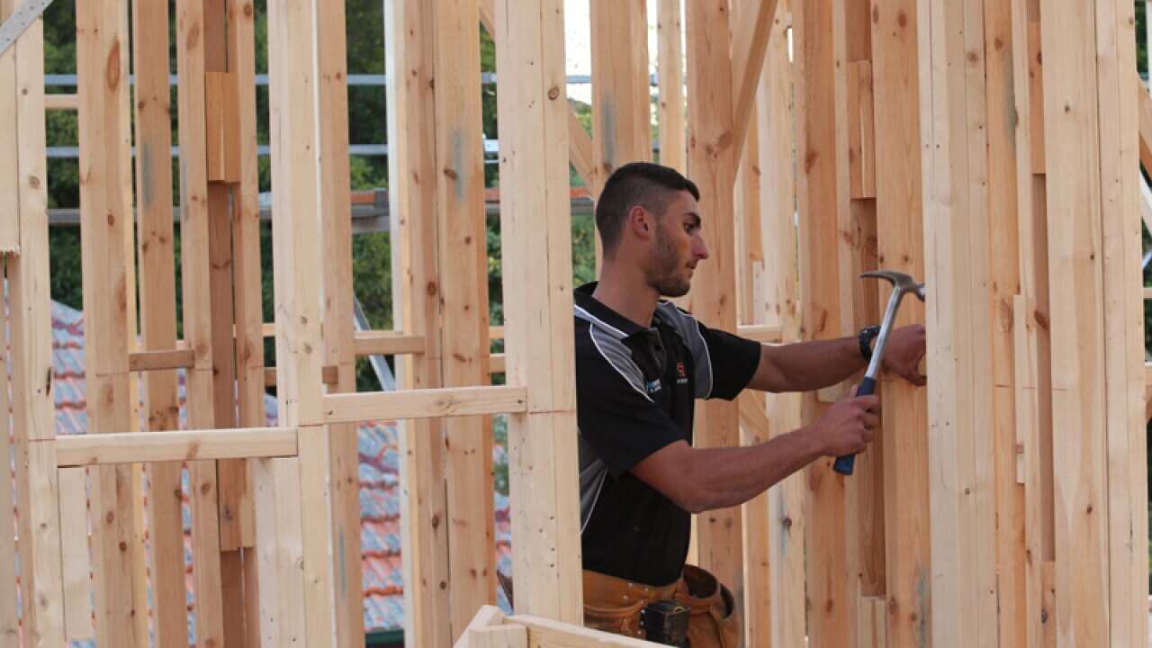 A labourer works on the timber frame of an unbuilt house