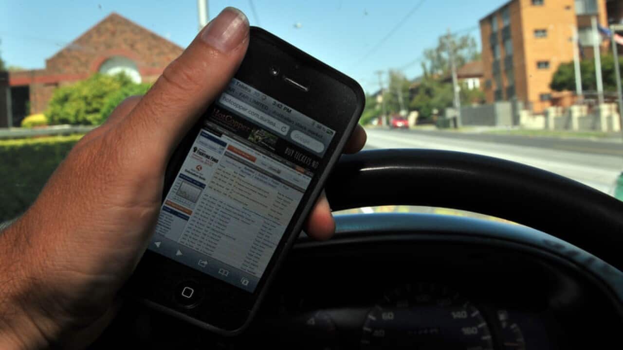 A driver holds a mobile phone whilst driving in Melbourne, Friday. Jan. 3, 2014. (AAP Image/Julian Smith) NO ARCHIVING