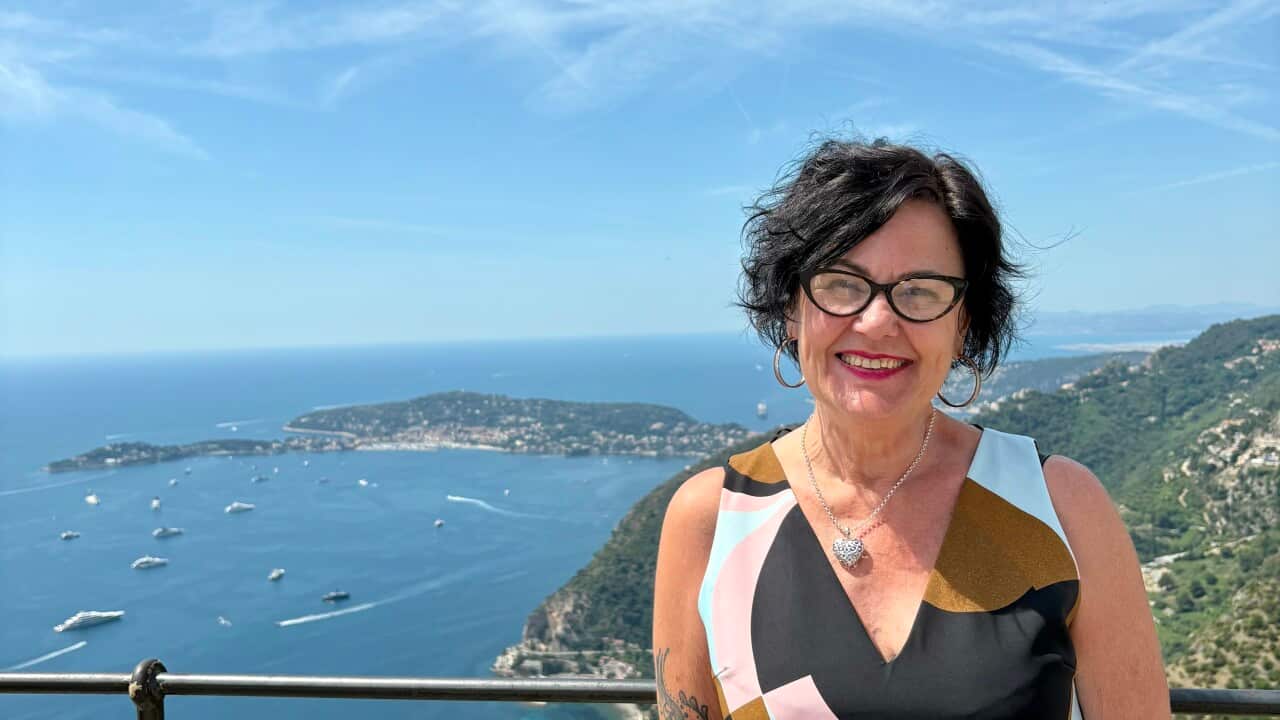 A smiling, middle-aged woman posing atop a hill with views of a waterway in the background.