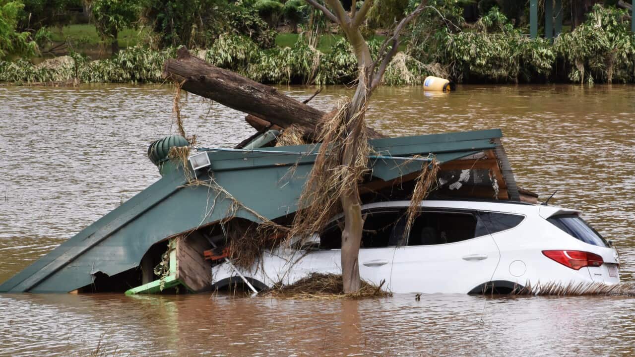A white car in floodwaters with debris pon top of it