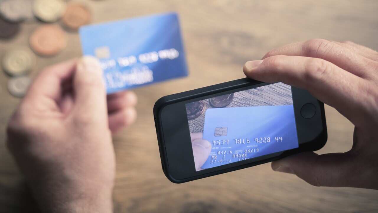 A person takes a photo of their credit card on their mobile phone to send to a scammer.