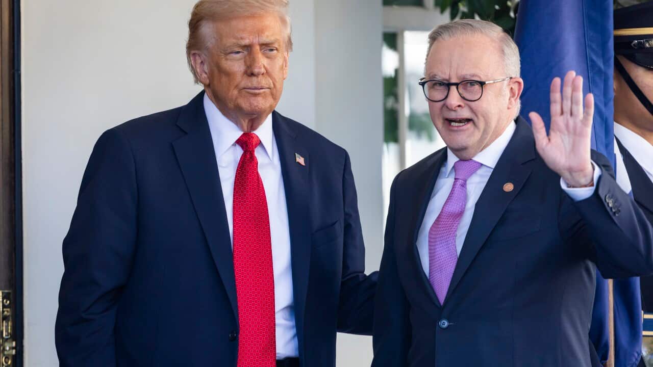 Donald Trump standing next to Anthony Albanese, who is waving a hand. They are in front of a white wall.