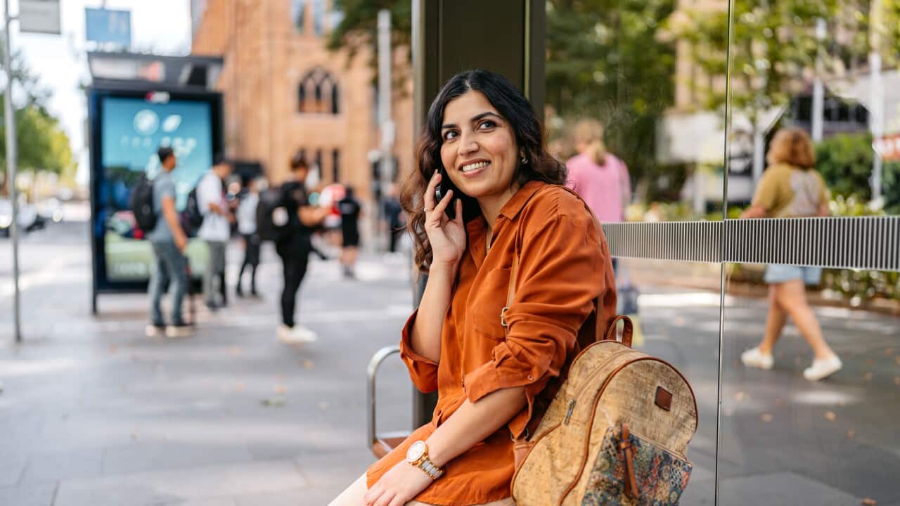 Mid-Adult Indian Woman Talking On The Phone While Waiting For A Bus At The Bus Station In Sydney In Australia