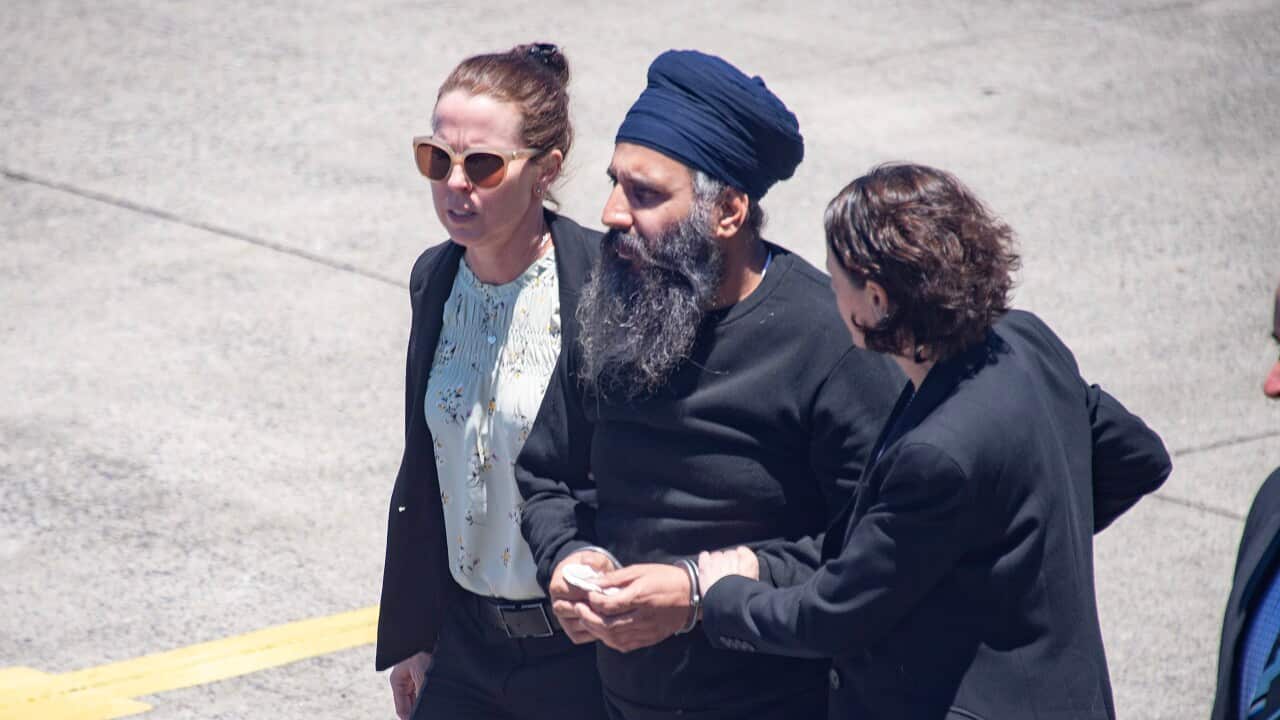 An Indian Sikh man in handcuffs is being escorted by two female police officers in civil clothes off a plane.