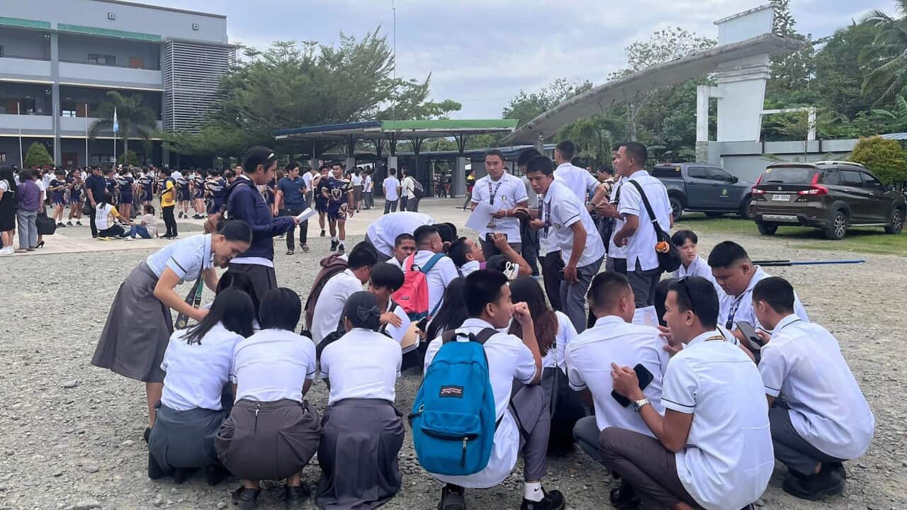 A group of school students crouching on the ground outside school buildings following an earthquake in the Philippines.