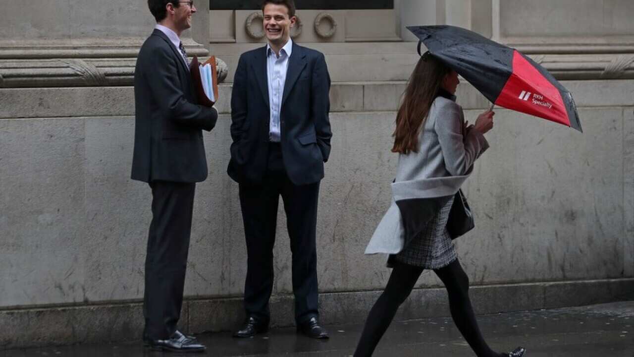 A woman shelters from the rain beneath an umbrella as she walks past talking men