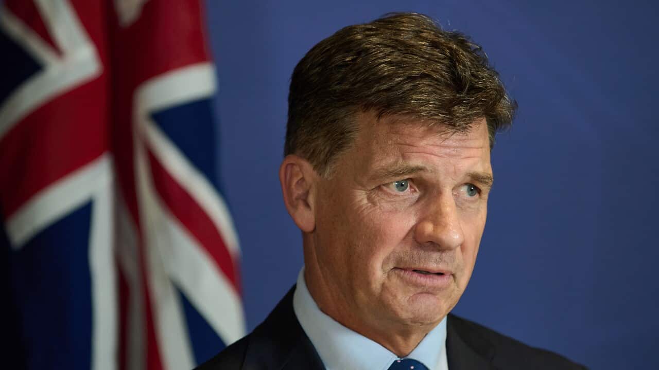 A man in a suit and tie, with the Australian flag blurred in the background.