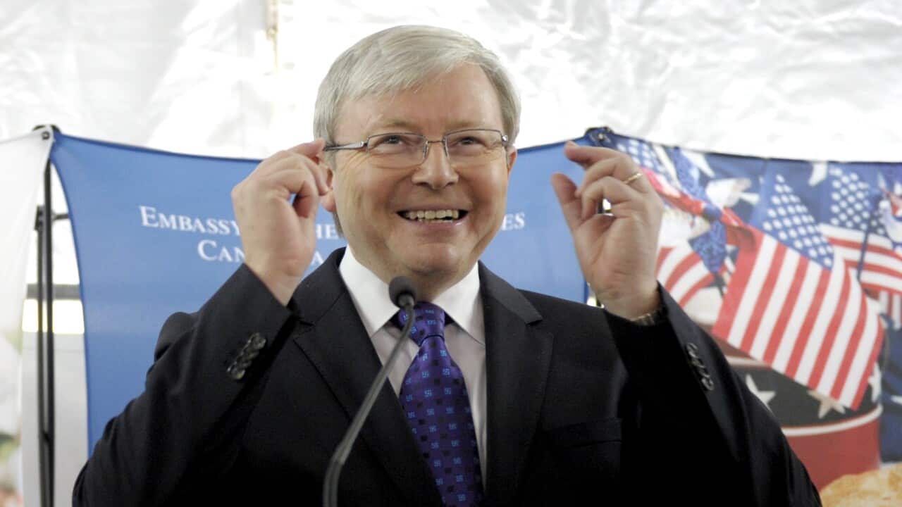 A man smiles as he raises his hands in the air. There are American flags in the background.