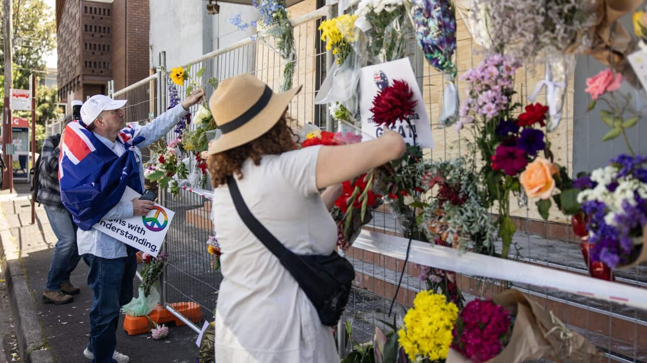 Two people placing flowers on a wire fence outside the synagogue.