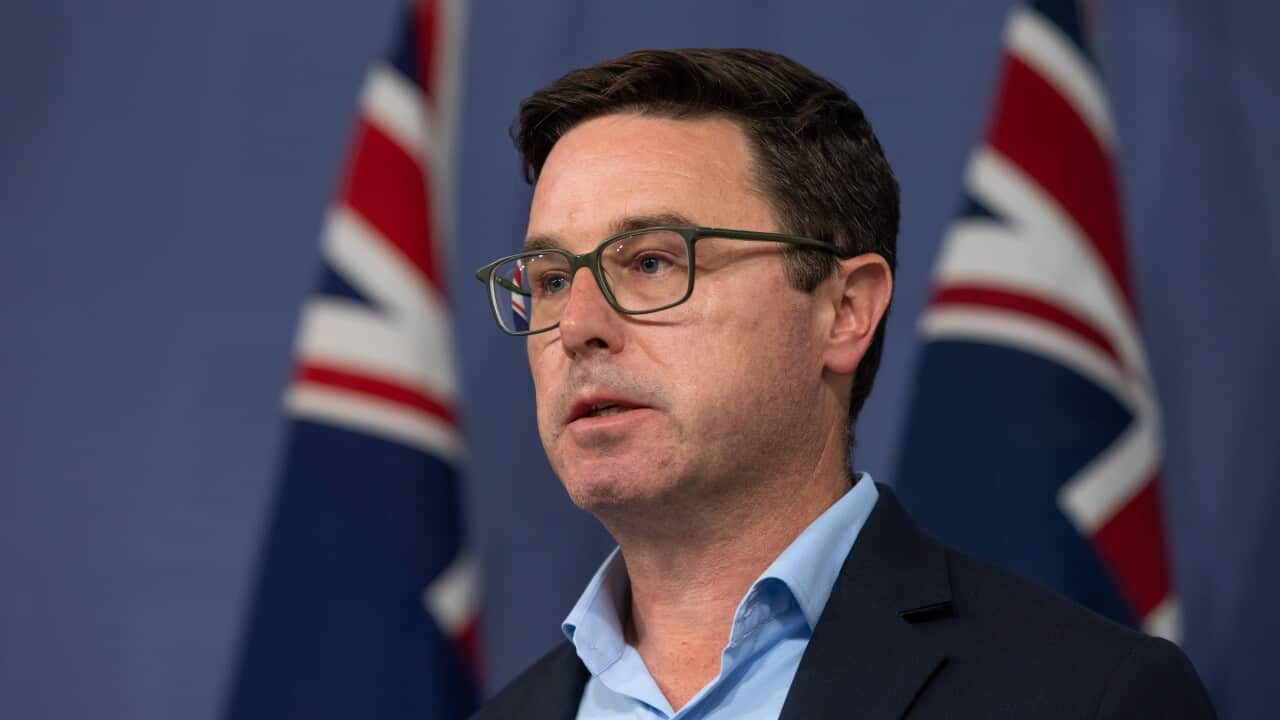 A man in a suit in front of Australian flags