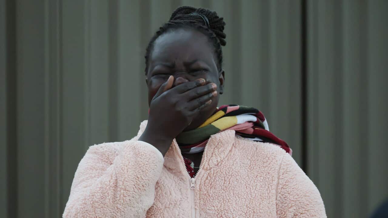 A woman in a pink jacket cries clasping her hand over her face