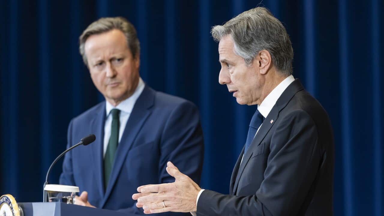 A man in a navy suit and a man in a black suit standing in front of a blue curtain