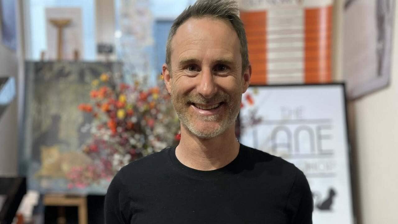 Author Craig Silvey stands in a bookstore smiling while holding two of his books, Runt and Runt and the Diabolical Dognapping.