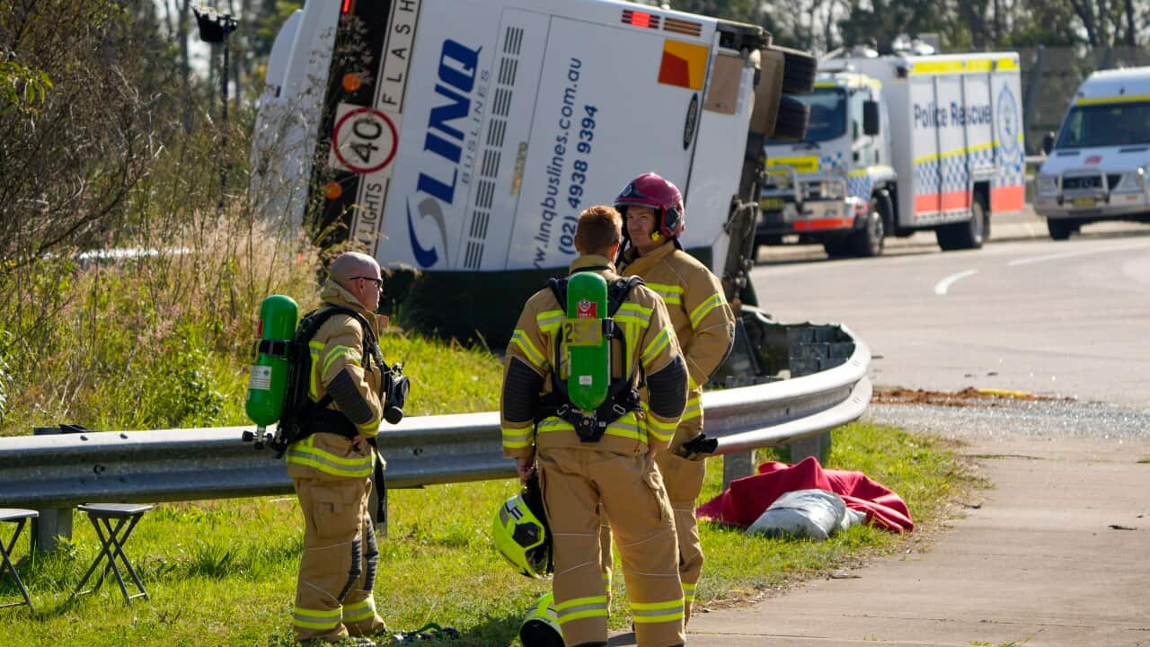 Emergency crew members stand near an overturned bus on the side of a road.