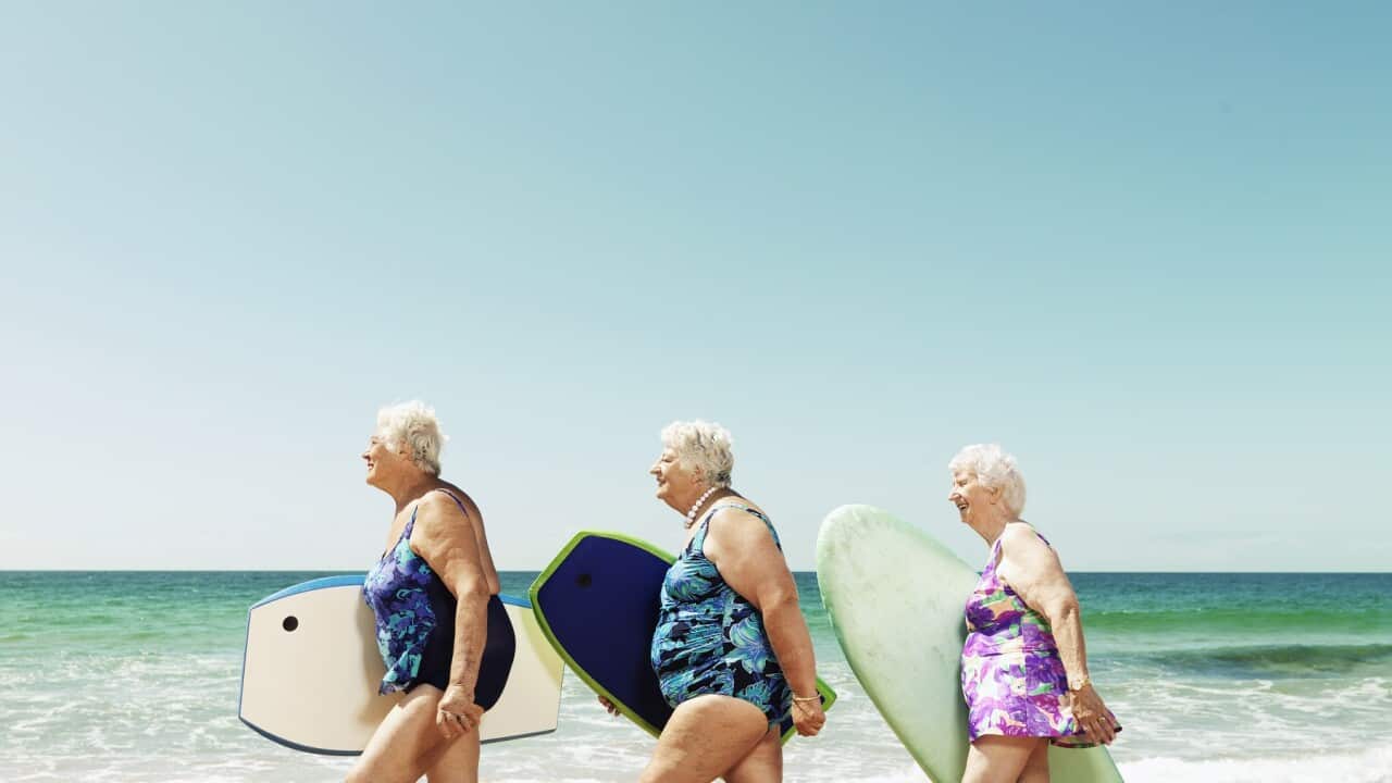 Three mature women on beach with surfboards