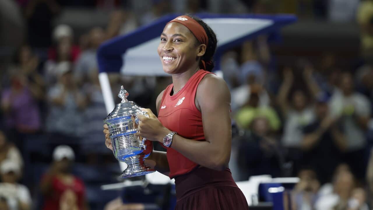 A woman in a tennis uniform holds a trophy smiling