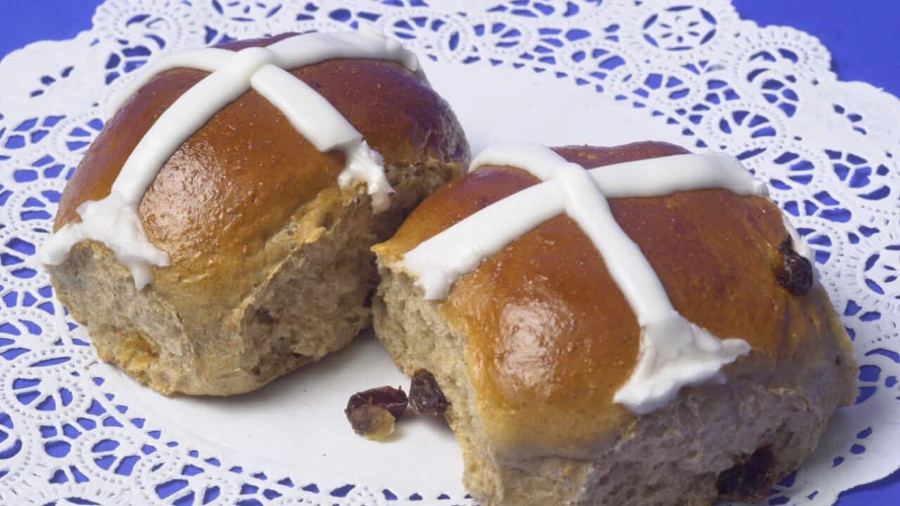 Two hot cross buns on a white tablecloth