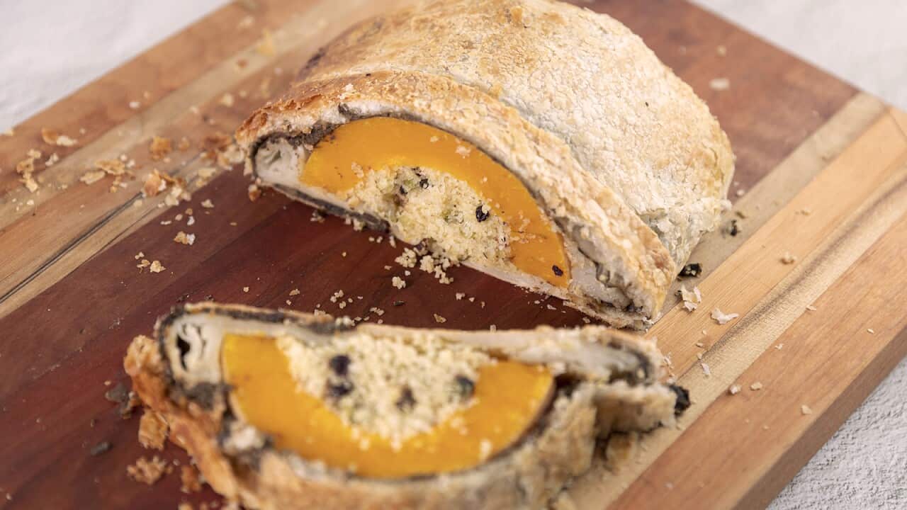 A golden pastry parcel sits on a wooden board. It has been cut open to show an arch of pumkin with a current-studded stuffing.