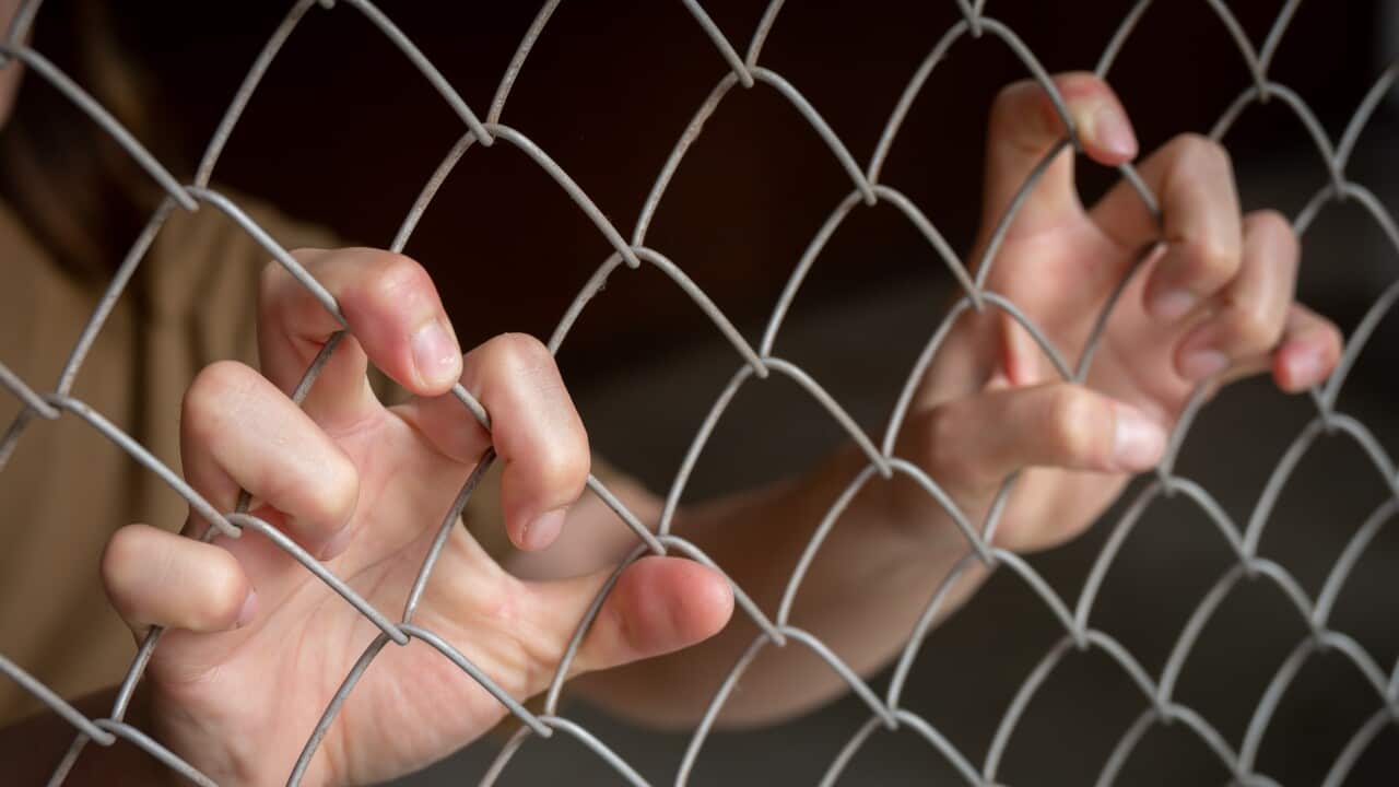 Cropped shot view of woman hands gripping on a metal wire fence.