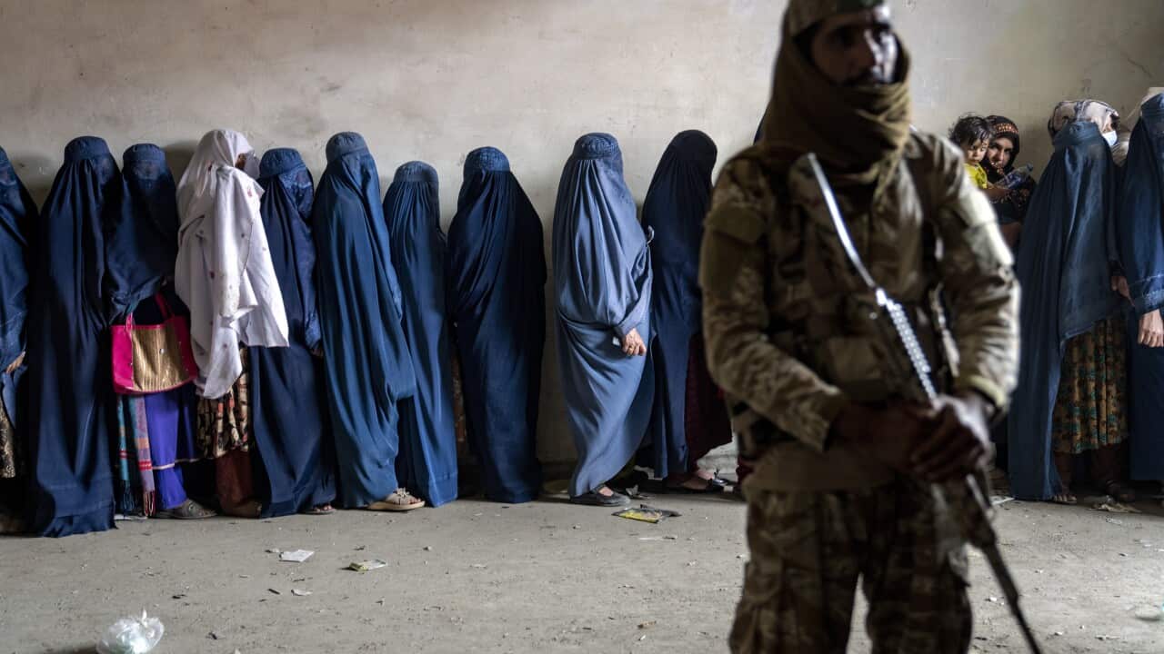Women wearing the Afghan chadri line up behind fighter holding firearm.