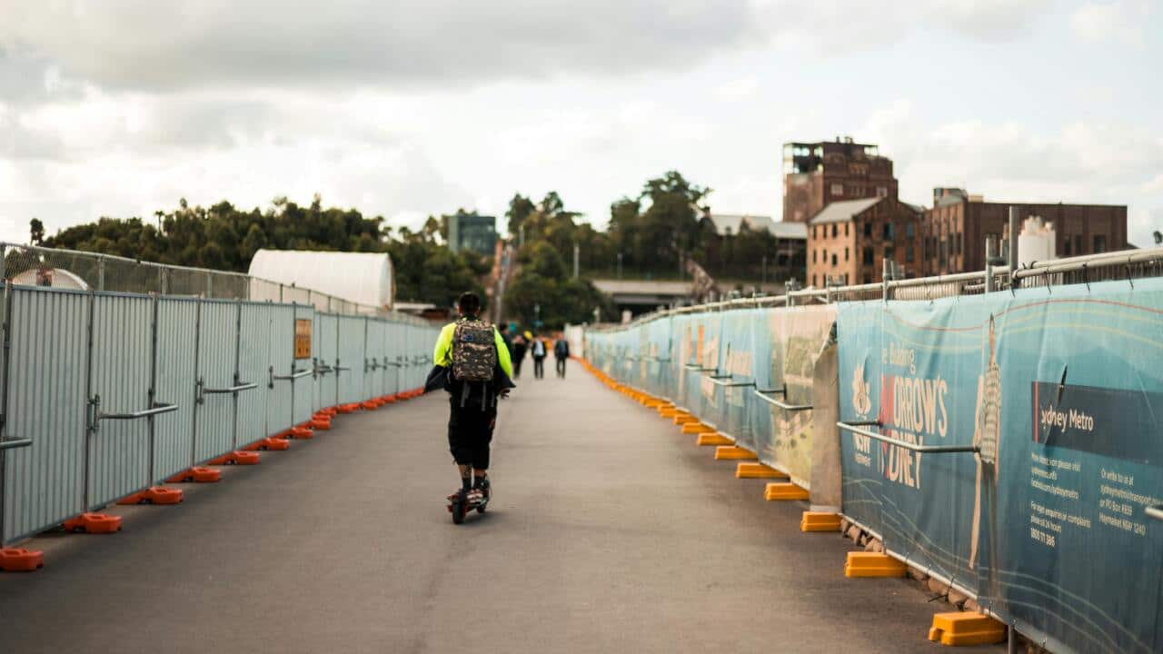 A man riding a scooter in Sydney around a construction site.
