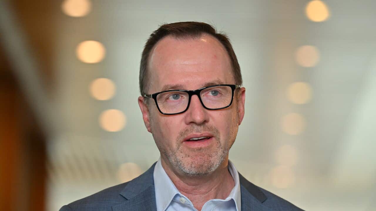 A man in a grey suit and glasses is speaking.