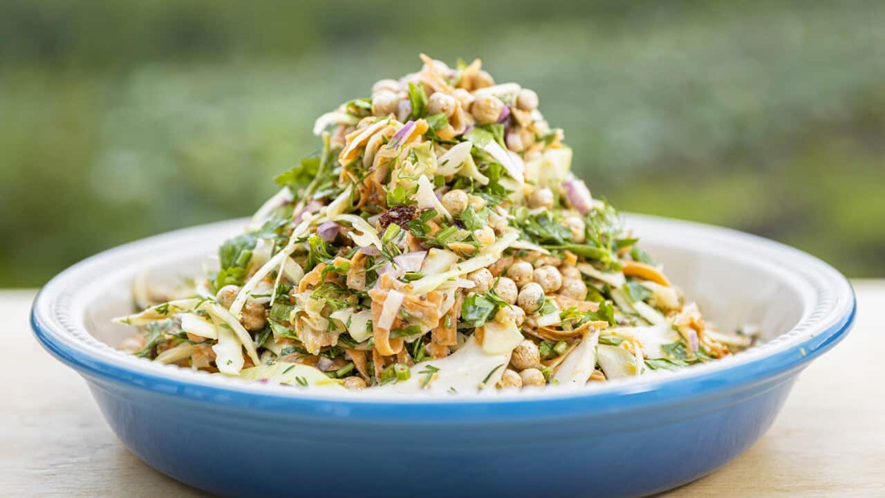 A pile of colourful cabbage, herb and chickpea salad sits in a bright blue serving dish on a wooden table.
