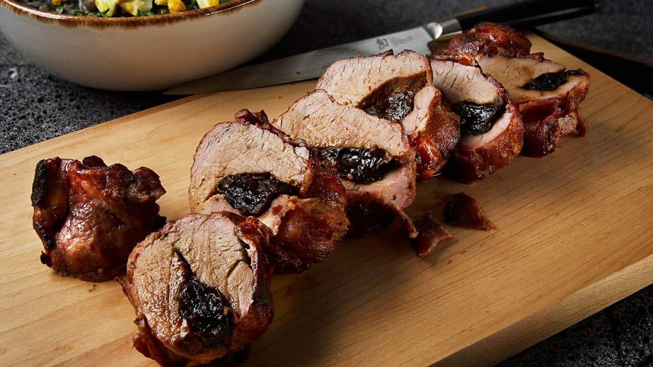 A cooked, juicy pork loin, cut into slices that show the prune stuffing, sits on a wooden board.