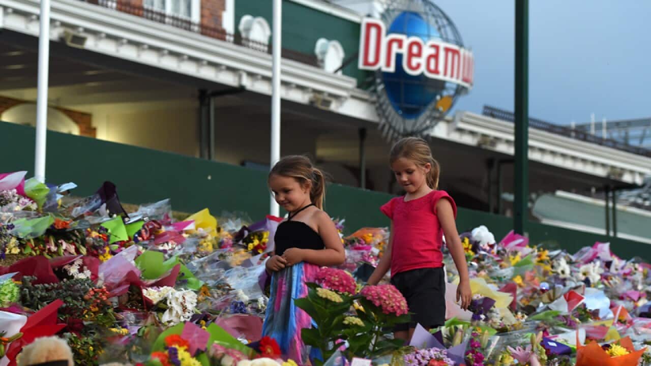 Young girls walk through a floral tribute outside Dreamworld