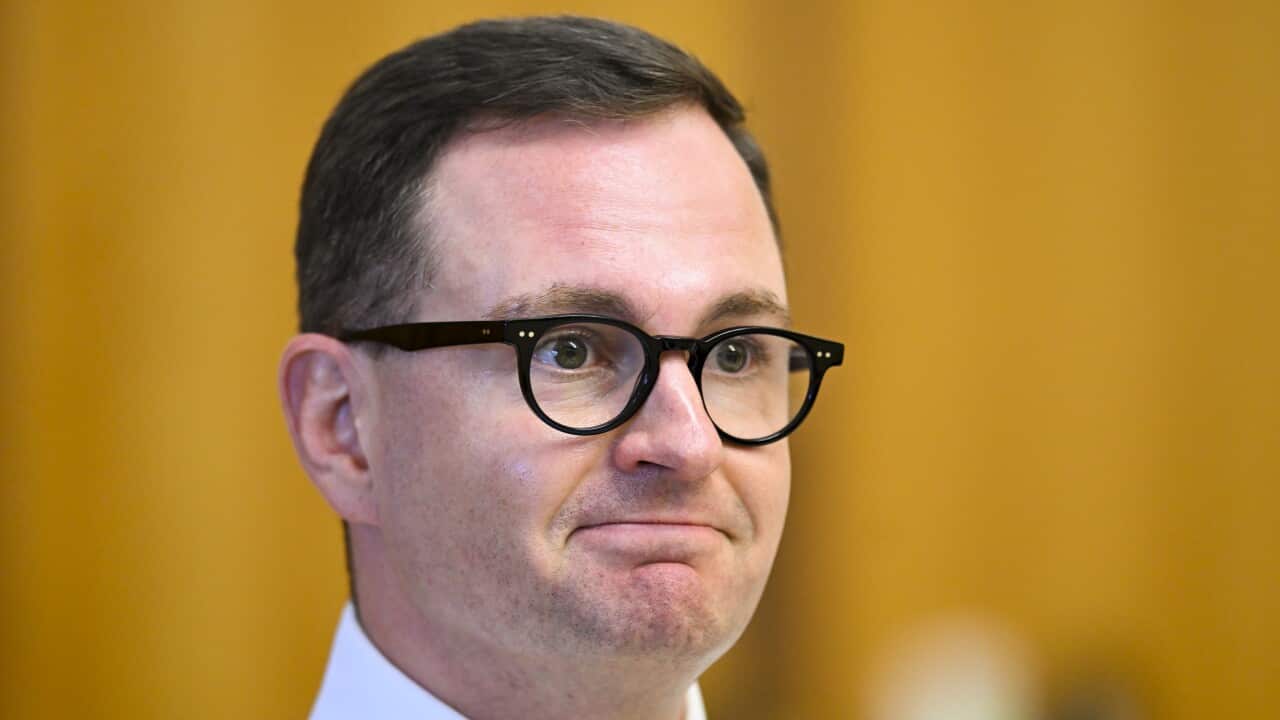A man wearing a white shirt and glasses is listening while seated.