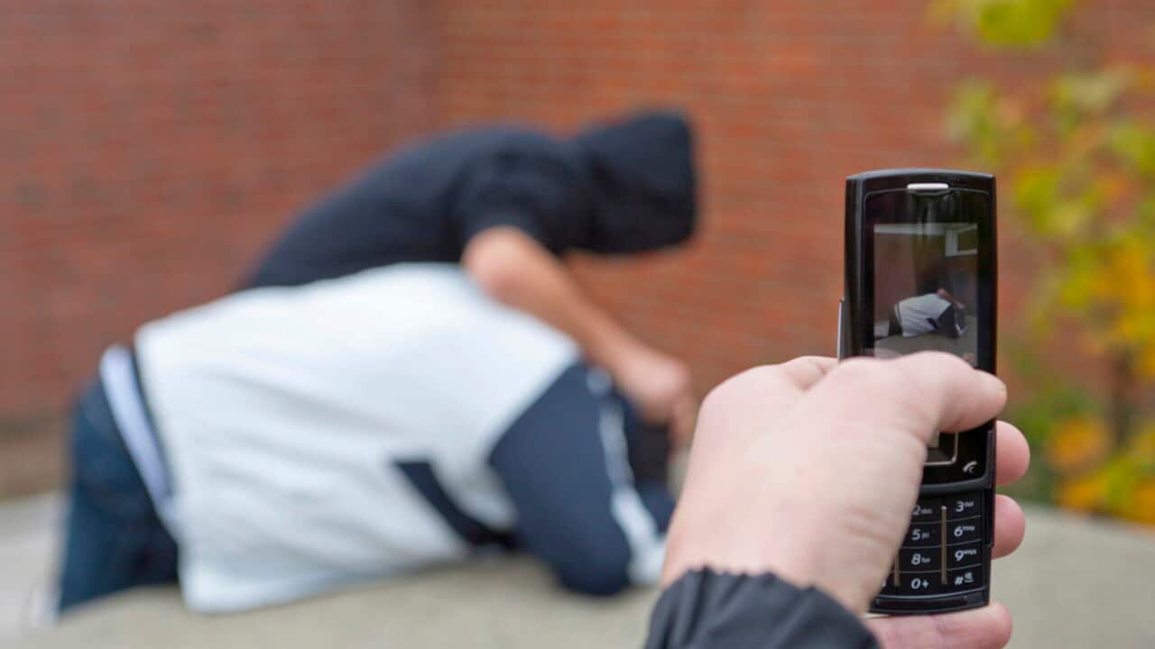 Boy pushing another boy down onto a table tennis table being filmed with a mobile phone