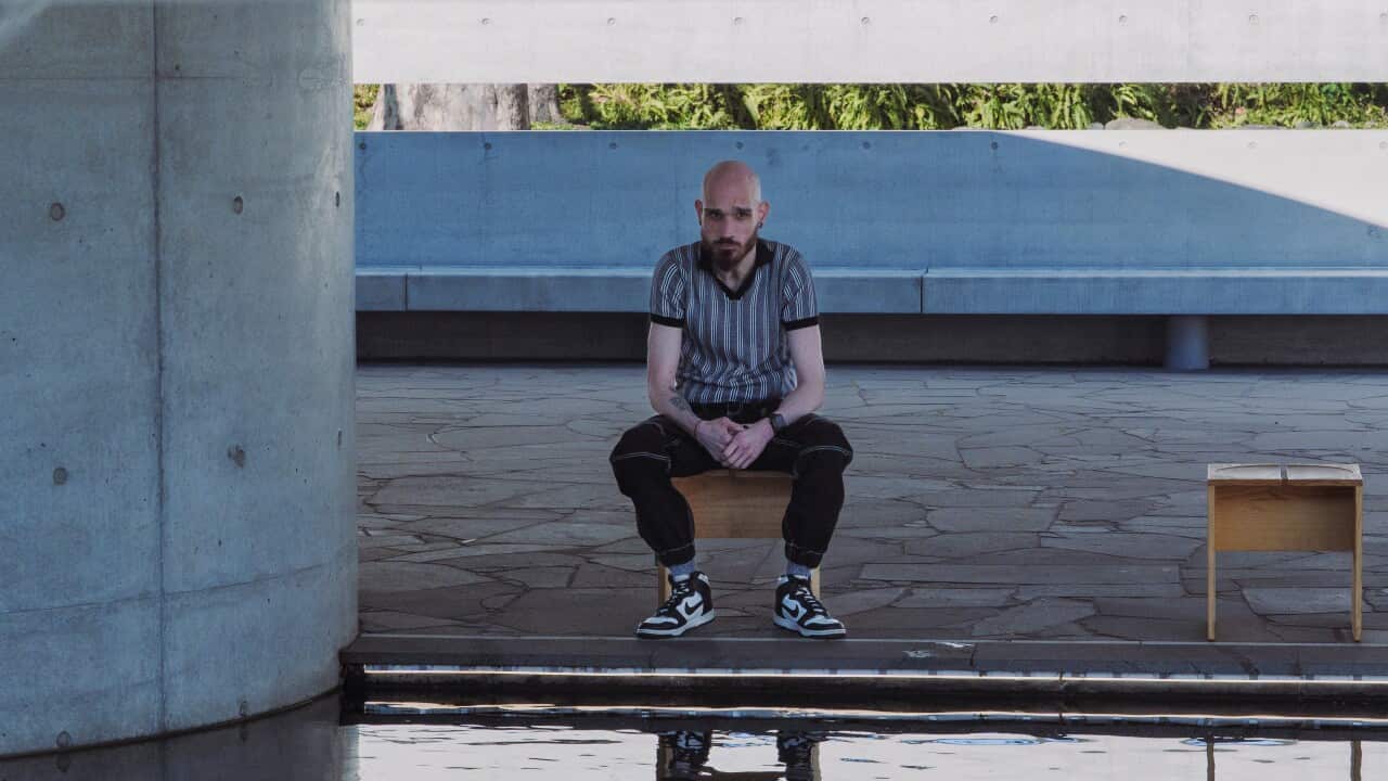 A man sits on a wooden bench in an outdoor area. 
