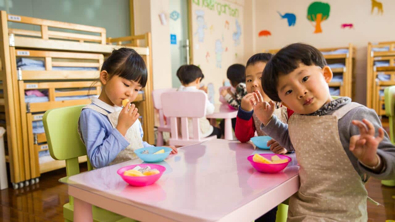 Three toddlers eating on white table.
