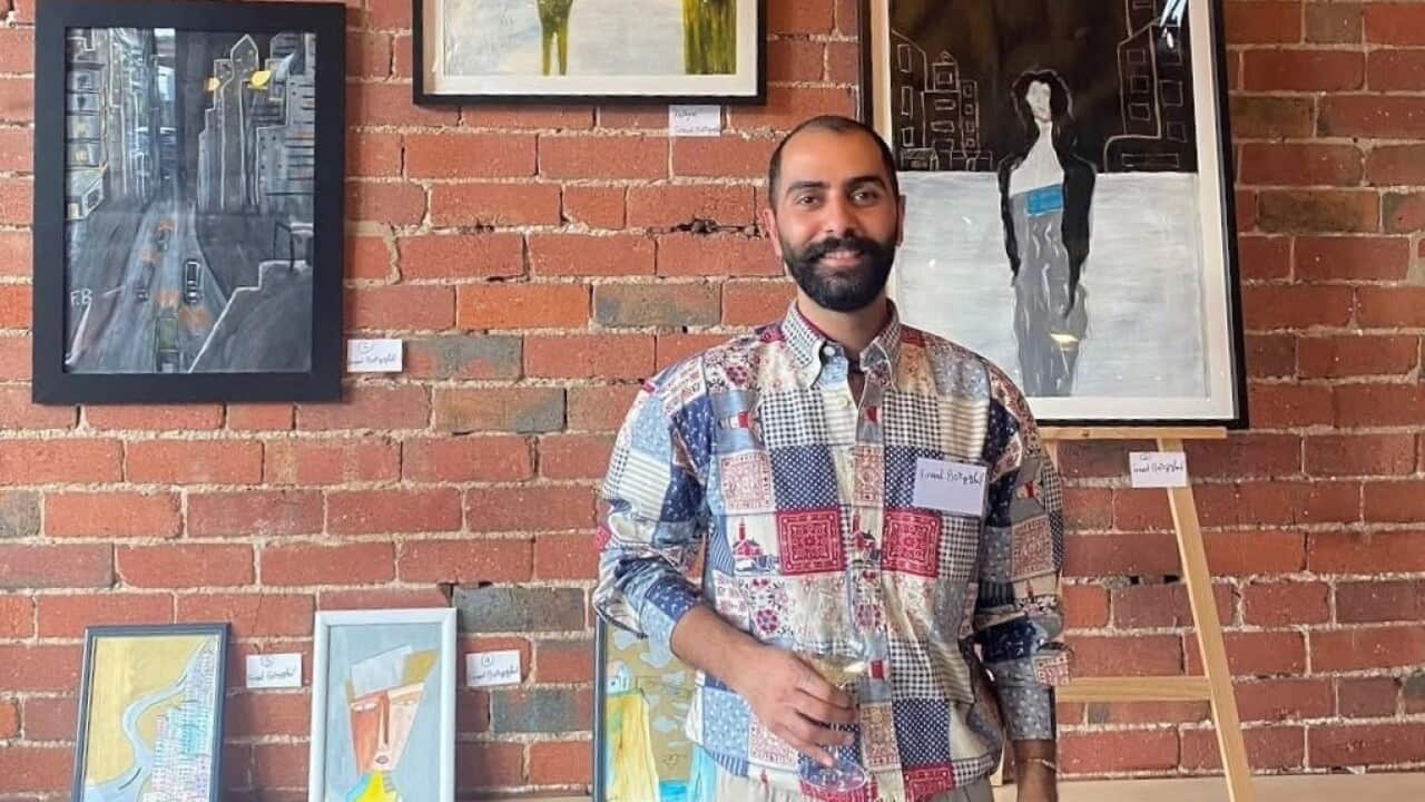 A man in a colourful shirt smiles to camera. He is standing in an art gallery